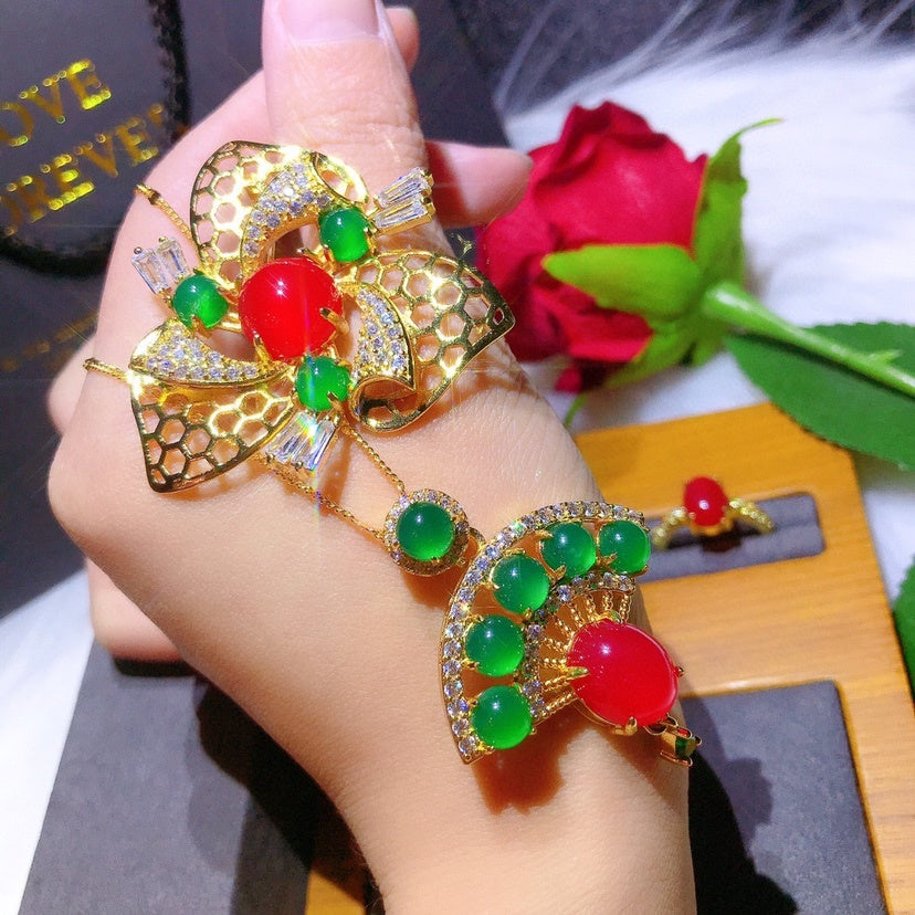 Gold ring with red and green gemstones on a hand, with a rose in the background.