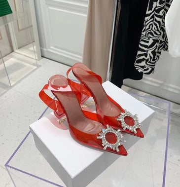 Red high-heeled shoes with decorative elements on a white platform.