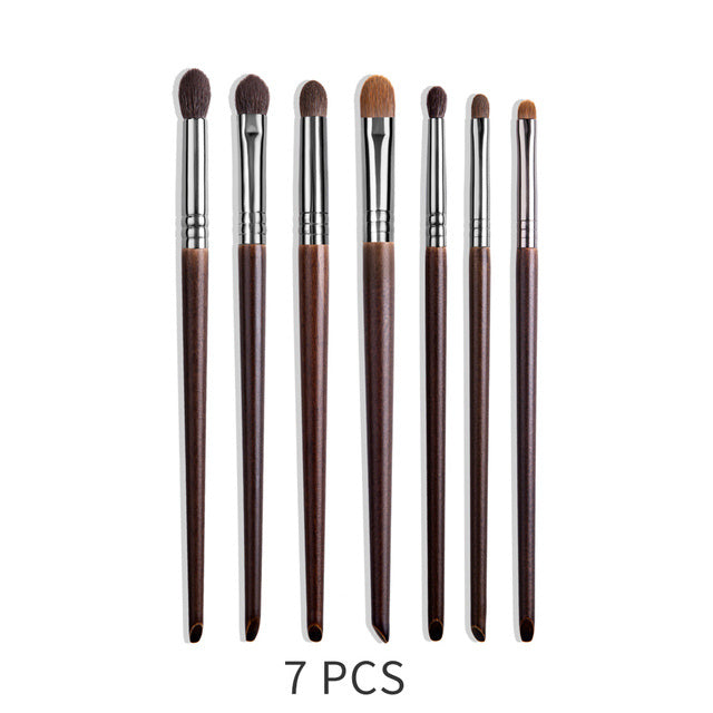 Set of 7 makeup brushes with brown handles and silver ferrules on a white background.